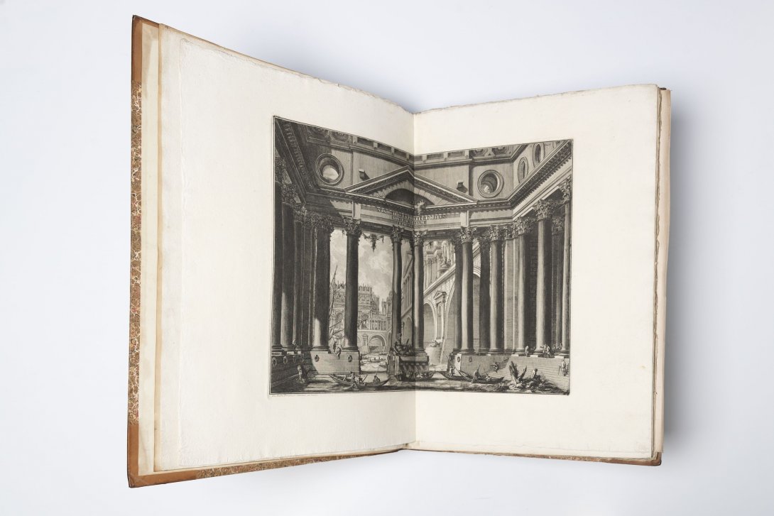 An old book open to show a two page spread of black and white engraved entrance with large stone pillars.