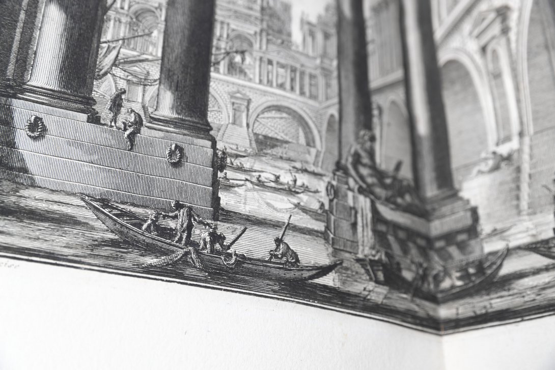 A close up of a black and white illustration a boat with people inside docked at a harbor at a roman styled city.