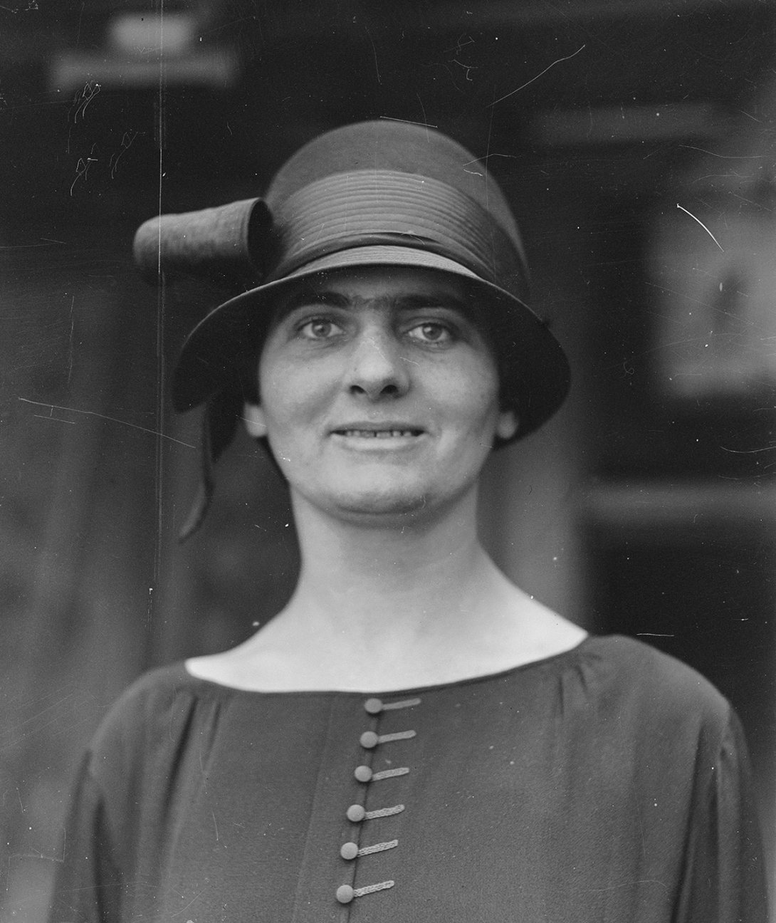 A black and white image of a woman wearing a bowler style had with a bow looking at the camera