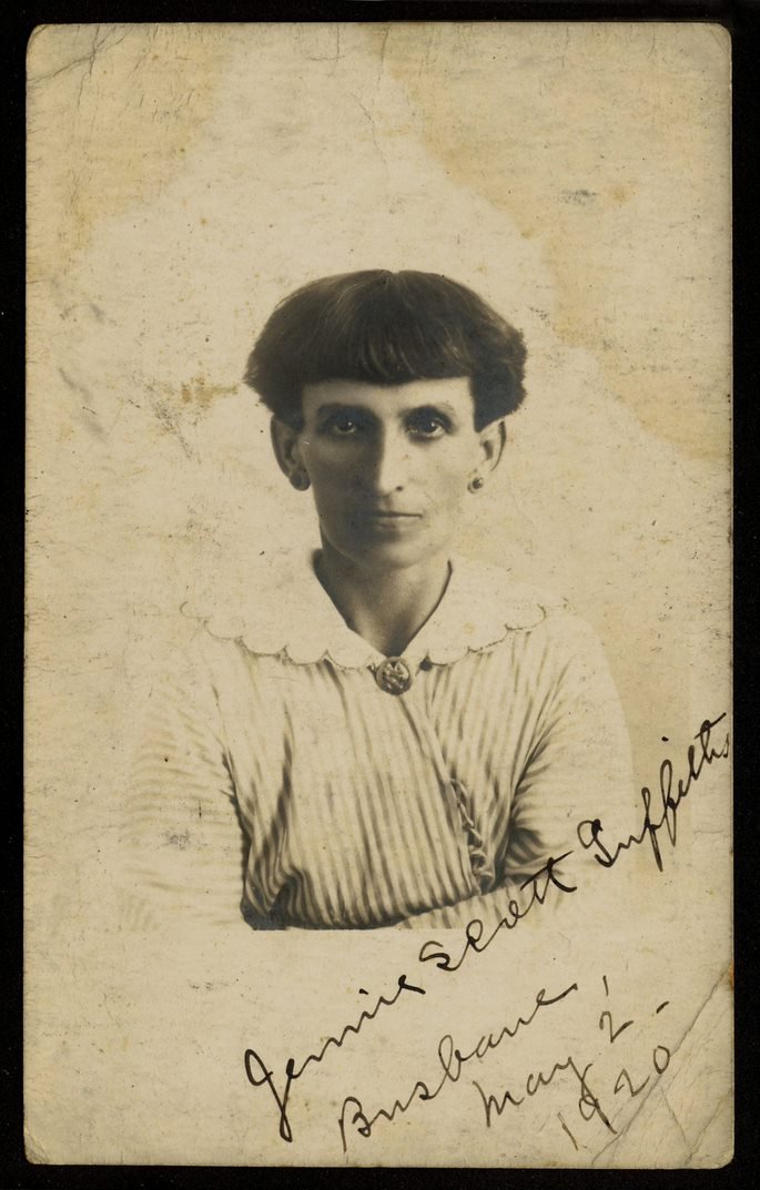 A old fashioned sepia image of a woman leaning on her crossed arms looking at the camera. There is hand written cursive text at an angle in the right corner. Text: ''Jennie Scott Griffiths, Brisbane, May 2, 1920'.