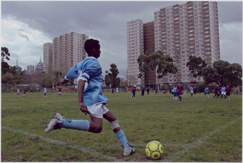 A boy kicking a soccer ball from the corner of a soccer field for a 'corner cross'.