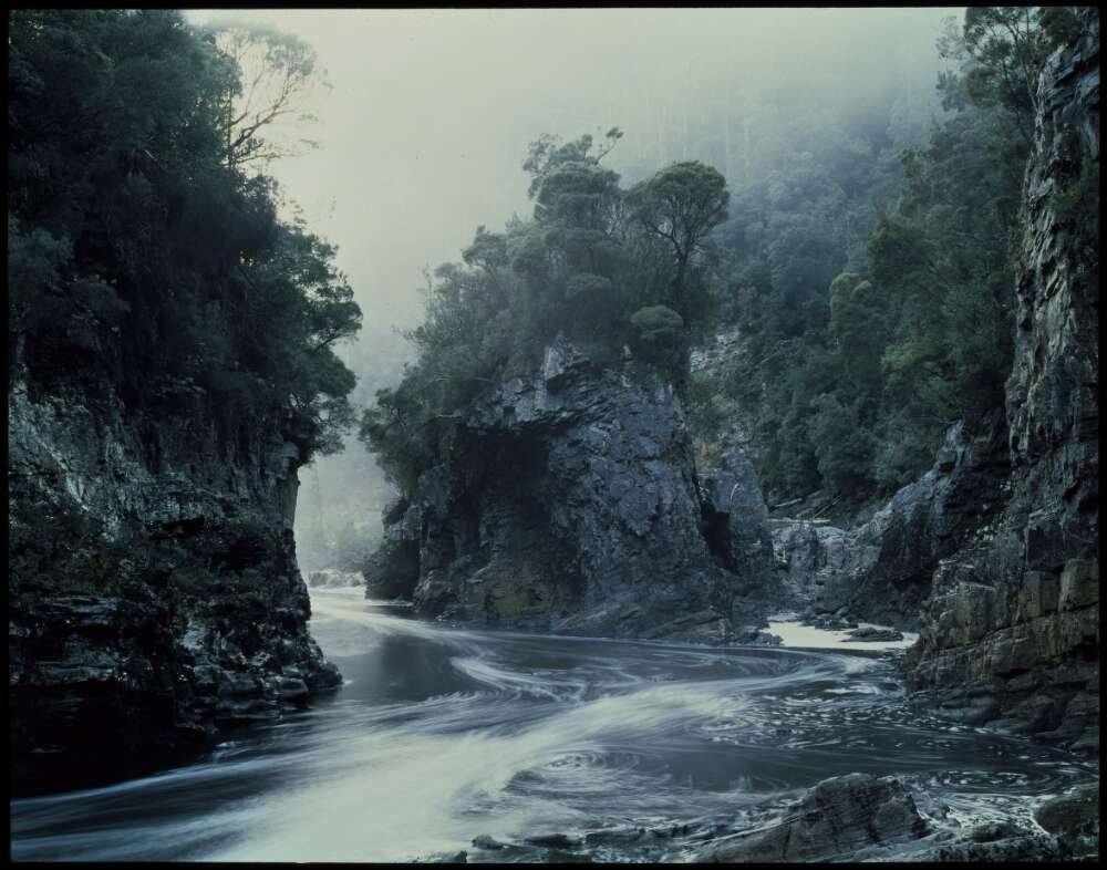 A river running through the green mountainsides with mist covering the top.