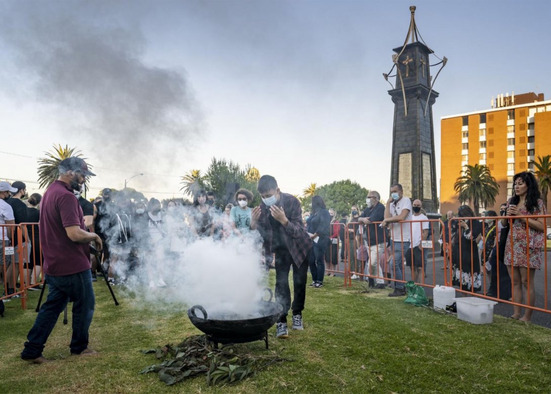 Many people gathered on some grass watching a traditional First Nations smoking ceremony