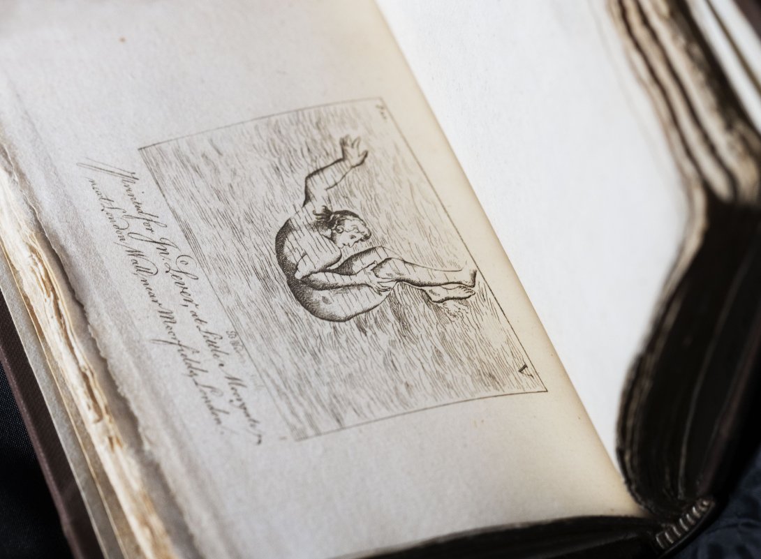 A rare book about swimming held open. Left side shows a person underwater in a curled position with some cursive text too small to read while the left side is blank.