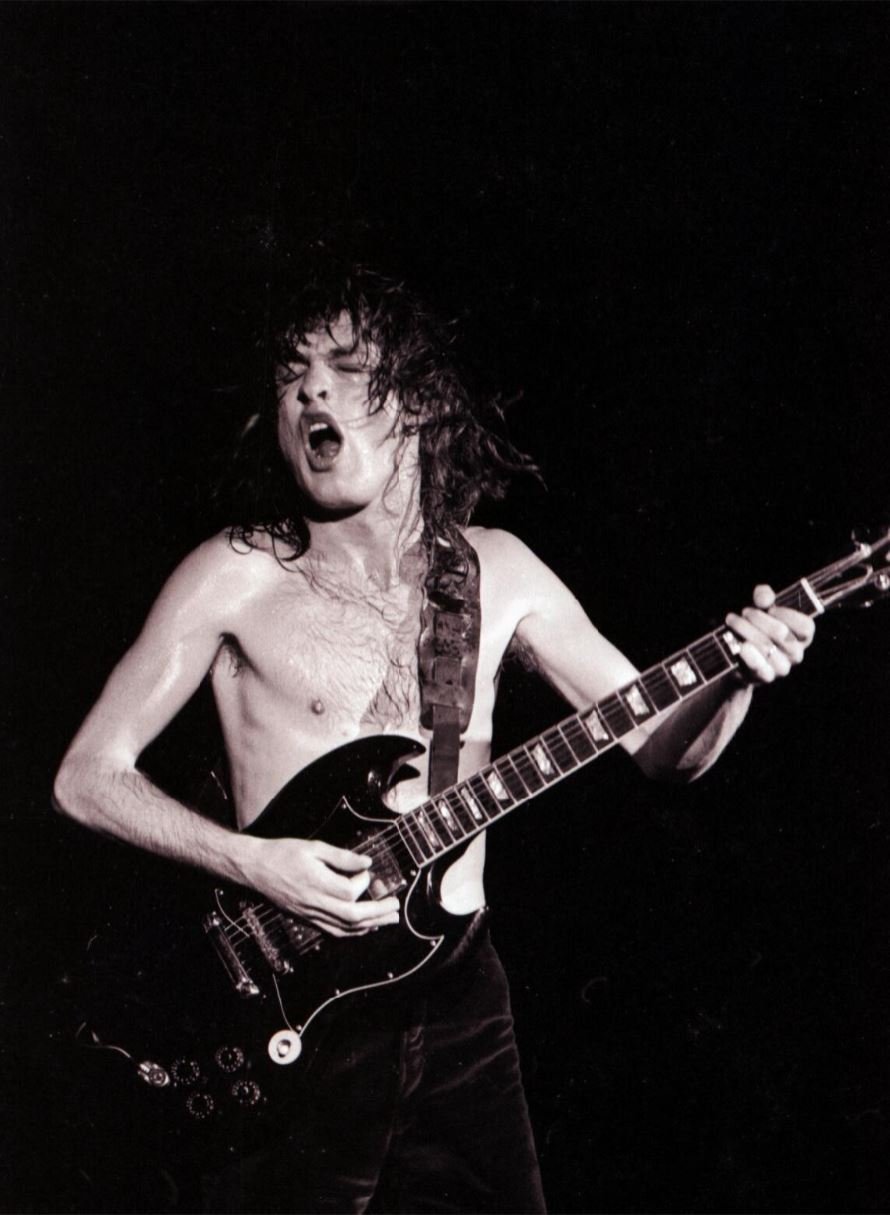 A black and white image of a man with long hair, wearing no shirt, playing guitar
