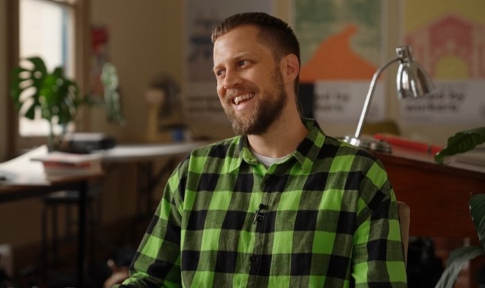Man with short brown hair and beard in checkered green and black button-up shirt smiling