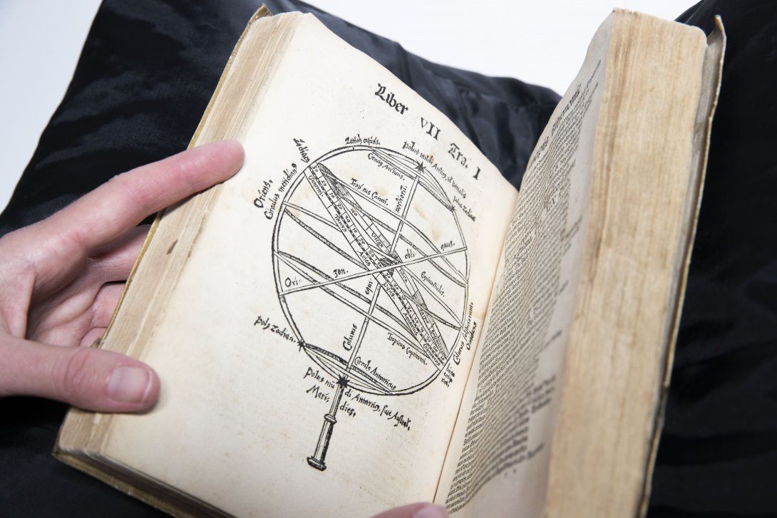 A rare book being held open to a page with an illustration of a circular device.