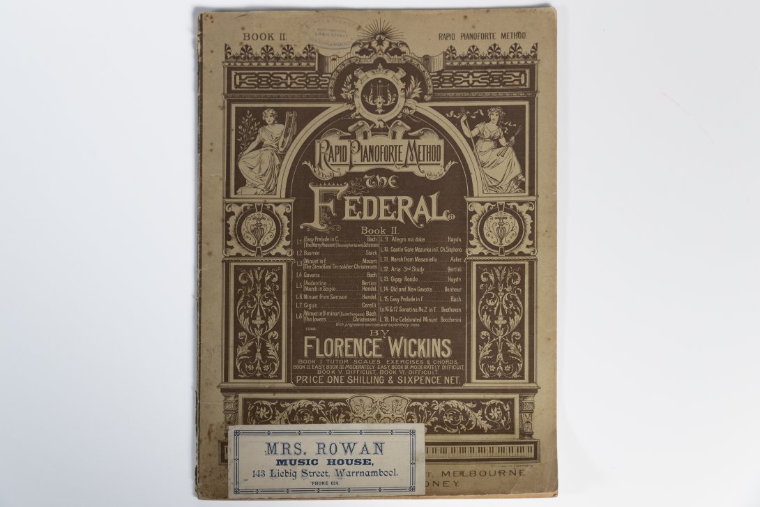 Closed music book with ornate cover and a sticker at the bottom left hand corner.