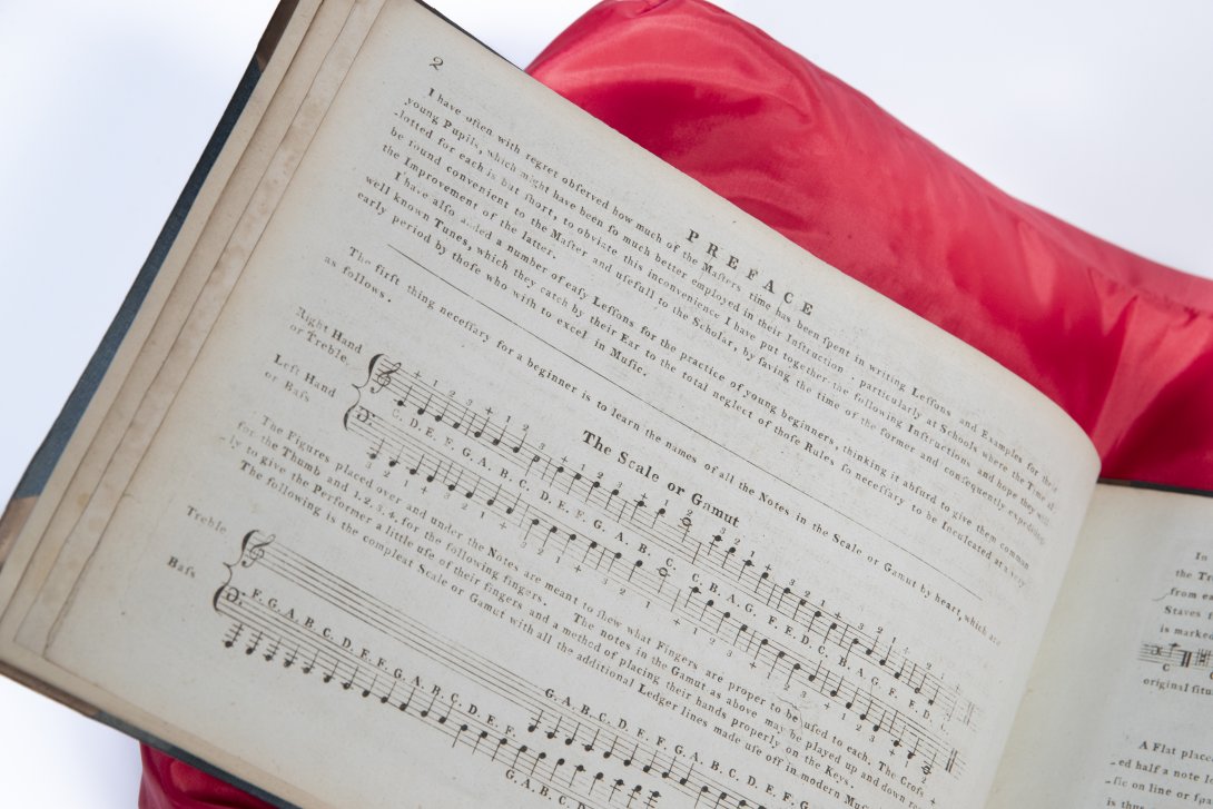 Open musical text book with left hand page visible, sitting on a red cushion. Partially obscured.