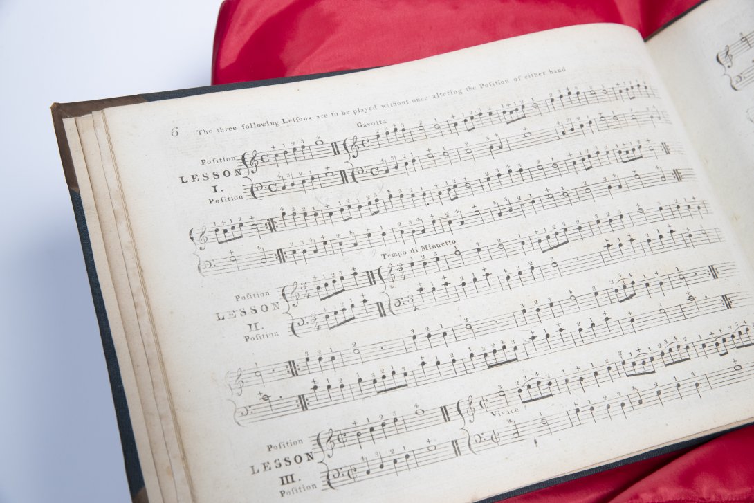 Left hand page of a musical score sitting on a red cushion. Partially obscured.