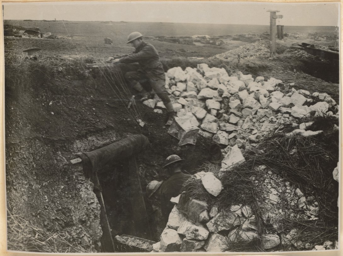 Soldiers in dugout near an entrance, one higher up so that his head sticks out of the dugout