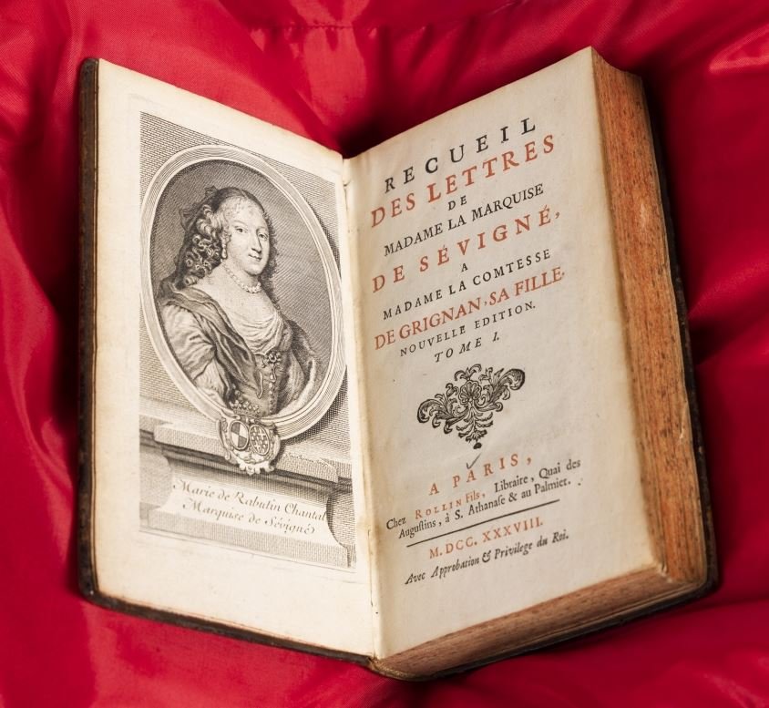 Photo of a rare book on a red cushion featuring a portrait of a 17th-century woman on the left and title page on the right