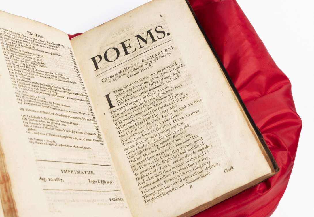 Photo of an open rare book on a red cushion with 'POEMS' in large letters on the right hand page