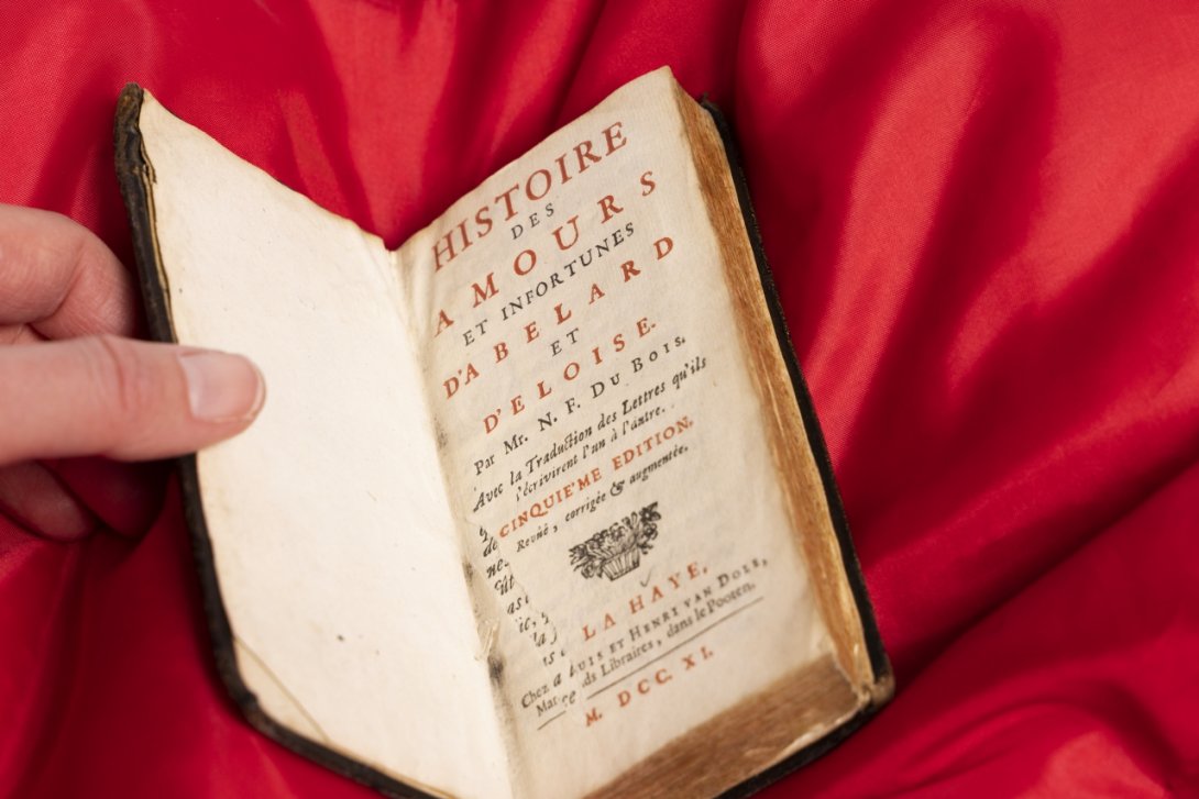 Photo of a rare book on a red cushion with a title page of the right, with red and black text