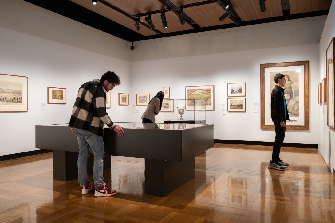 Three people looking at items in display cases and on the walls of a gallery space