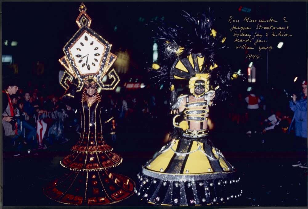 Two men in elaborate costumes, one as an antique clock and the other with yellow and black stripes, walking down a street during a parade 