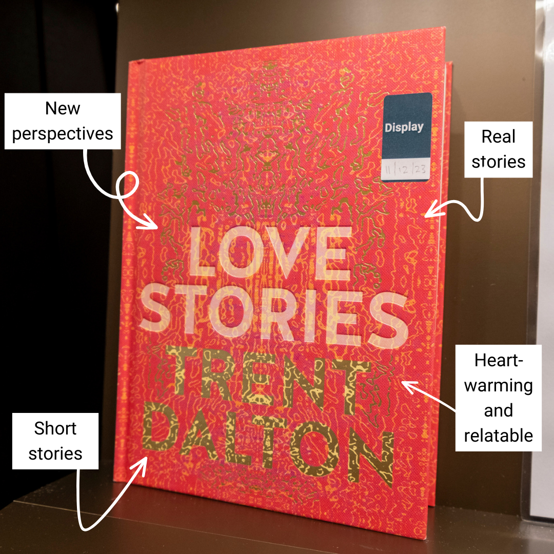 Hardback book with patterned red cover with text reading 'Love Stories' and 'Trent Dalton' sitting on display on a shelf. Around the book are annotated reading 'new perspectives', 'heart-warming and relatable', 'real stories' and 'short stories'.
