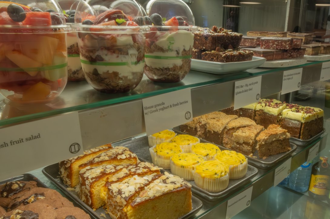 Cafe display of cakes, slices, fruit cups and granola cups