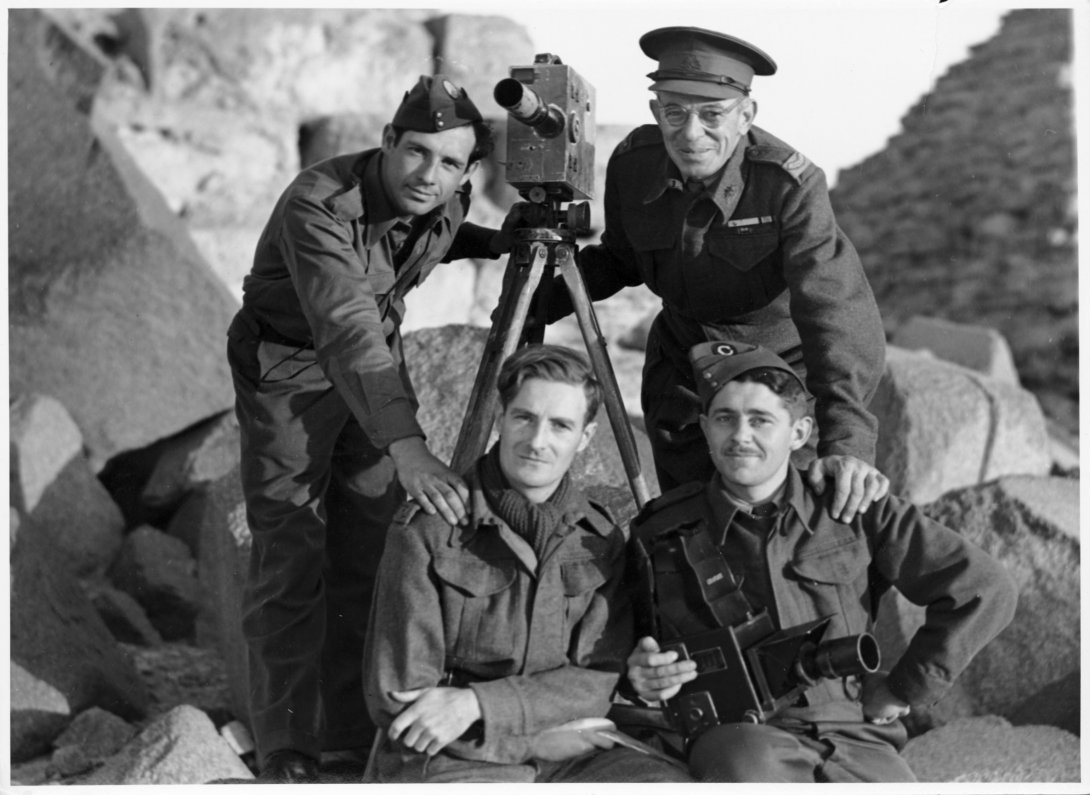 Four men of various ages in military dress around an old video camera